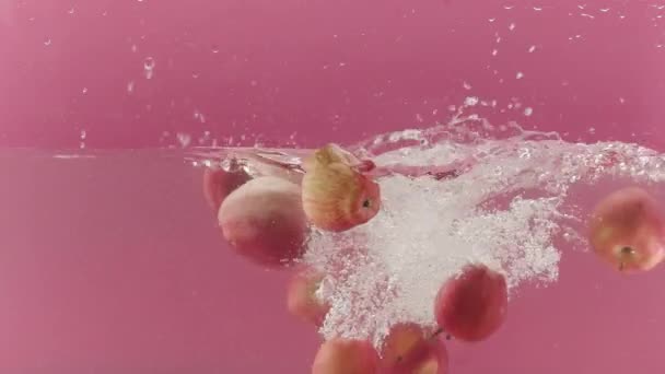干净的水 掉下整个苹果 一堆堆鲜红苹果和水流缓缓流入透明玻璃杯 清澈的水和粉色背景的苹果 — 图库视频影像