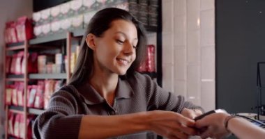 Gündelik giysiler içinde uzun siyah saçlı pozitif bayan müşteri sipariş için ödeme yaparken modern kahve dükkanında kredi kartıyla ulaşılamıyor.