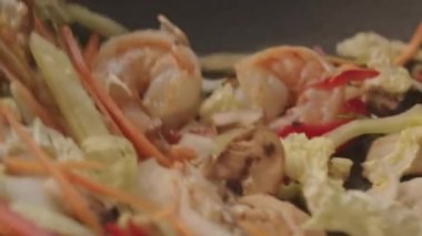 Tavada etli sebze ve karides karıştırmak. Marulu mantarla havucu karides ve tavada pişirilen tavuk parçalarıyla karıştırmanın yavaş çekimleri.