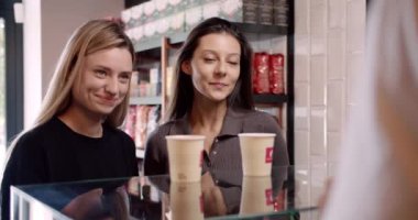 Tarlada tanınmayan baristalar, neşeli genç bayan müşterilere kahve dağıtırlar. Kredi kartıyla ödeme yaparlar ve kafede gülümserler.