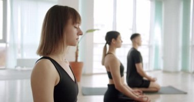 Gyan Mudra ve Thunderbolt 'ta meditasyon yaparken ışık stüdyosundaki grup yogası sırasında gözlerini kapatan siyah aktif giysili sakin bir kadının el kamerasıyla çekilen pozu.