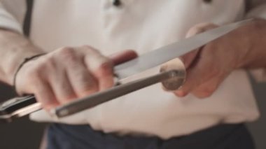 Şef 'in et kesmeden ya da yemek yapmadan önce serin bir bıçak keskinleştirdiği yakın çekim. Profesyonel aşçı iş için bir enstrüman hazırlıyor. Aşçı, evcil mutfakta bıçağını biler..