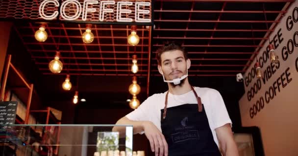 积极的年轻男性巴里斯塔微笑着 站在现代咖啡馆里看着相机 并展示了好的标志 年轻人在咖啡店工作的时候笑了 店主站在酒吧里 — 图库视频影像
