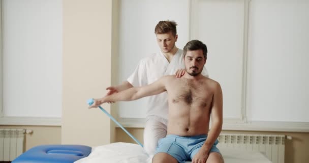 Programa Fisioterapia Hombre Hace Ejercicios Con Banda Elástica Con Ayuda — Vídeo de stock