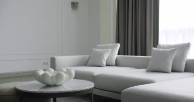 Beyaz, gri mobilyalı ve yuvarlak masalı modern Minimalist oturma odası. Köşedeki kanepe ve kitaplığı olan lüks modern ev iç mimarisi. Moda mobilyalar. Minimalist Ev İçi.