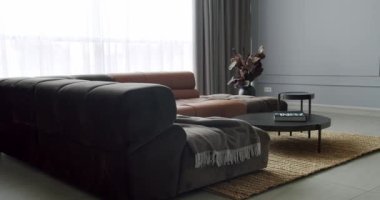 Gri ve kahverengi mobilyalı modern Minimalist oturma odası. Köşedeki kanepe ve yuvarlak masa. Moda mobilyalar. Minimalist İç İşleri. Konforlu Modern Mobilya Tasarımı.