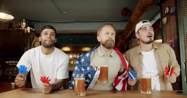 ファンはチームを失うことを心配している サポーターは彼らの最愛のチームに満足していません 米国の国旗を持つ男性はビールを飲んで スポーツゲームを見て — ストック動画