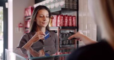 Gündelik giysiler içinde uzun siyah saçlı pozitif bayan müşteri sipariş için ödeme yaparken modern kahve dükkanında kredi kartıyla ulaşılamıyor.