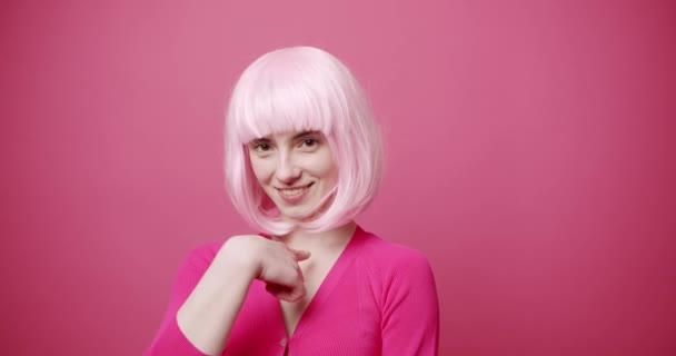 胸やカメラを指し 私はピンクの背景に笑顔でカメラを見ている間 私はあなたを愛して言うために心をジェスチャー明るい髪を持つ楽観的な若い女性の静的なショット — ストック動画