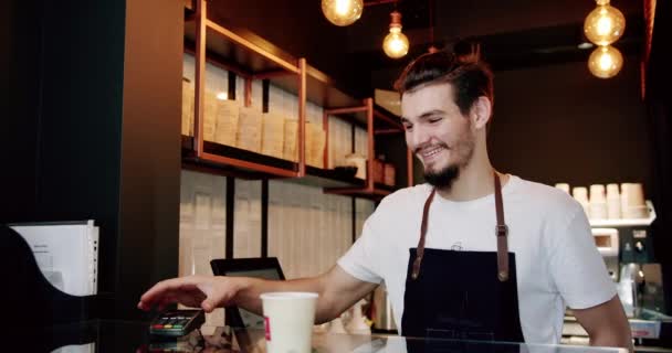 穿着白色T恤 留着小胡子 面带微笑的年轻而积极的男性巴里斯塔 一边在现代咖啡馆的柜台上端咖啡一边看着相机 一边看着镜头 — 图库视频影像