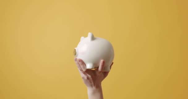 お金の箱を示すミステリー女性 黄色の背景を背景に腕を上げでセラミック貯金箱を実証匿名女性の静的なショット — ストック動画