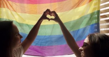 Destekleyen eller kalp işareti yapar ve gökkuşağı bayrağının önünde dalgalanır. Aşk işareti. LGBT 'nin kutlama etkinliği sembolü. Aşk Eşitliği. LGBT hakları. İnsan ilişkileri.