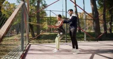 Dışarıda egzersiz yapan genç bir kız. Egzersiz yapan bir kadın. Spor salonu sağlığı konseptin dışında. Antrenör erkek, formda kadın egzersizleri yapıyor. Lastik bantlı kişisel antrenörle açık hava eğitimi.