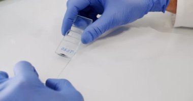 Crop scientist spreading colored sample on glass. From above anonymous scientist in latex gloves spreading blue liquid on glass on white table during work in laboratory