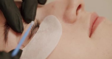 The master applies special glue before the eyelash curling procedure in pink rubber gloves close up. Woman eye with long eyelashes. Beautician eyelash extension for young woman in a beauty salon