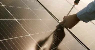 Crop Technician installing solar panels on metal stand. Technician connecting solar panel. Technician working with electrical screwdriver installing solar panel to metal platform system. Installation