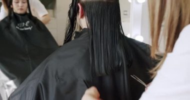 Woman cutting hair with barber scissors in beauty studio. Beauty and style concept. Barber makes a stylish haircut with professional scissors in a beauty salon. Hairdresser trimming brown hair.