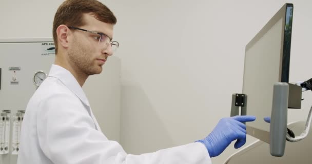 在临床工作中使用现代机器的手提式实验衣和手套检查试管及计算机拍摄 用电脑设备进行血液测试 验血机检查样本 — 图库视频影像