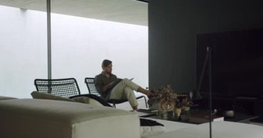 Man reading book in living room. Pan left view of relaxed male flipping page of book while sitting on chair and reading interesting book in modern lounge area