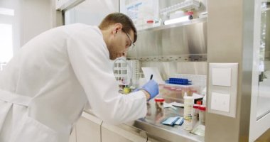 Scientific Lab for Medicine, Biotechnology Development. Handheld shot of man in white robe with gloves and glasses putting vial with sample into machine during work in medical laboratory in clinic.