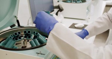 Male doctor places the blood tests in the centrifuge. From above centrifuge machine with test tubes spinning then stopping during workday in modern lab. Centrifuge machine with vials in laboratory.