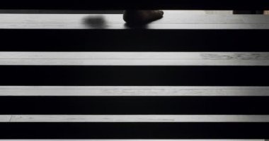 The man descends the stairs in the house from the second floor in the house and creates shadows and silhouette. Legs shot close up. black wooden stairs. modern apartment with black stair.