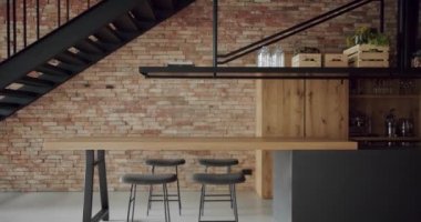 Modern and spacious wooden kitchen room with wall bricks and black staircase. Real Estate. Luxury kitchen with wooden island and chairs. Modern interior in luxury house. Minimalist design in New Home.