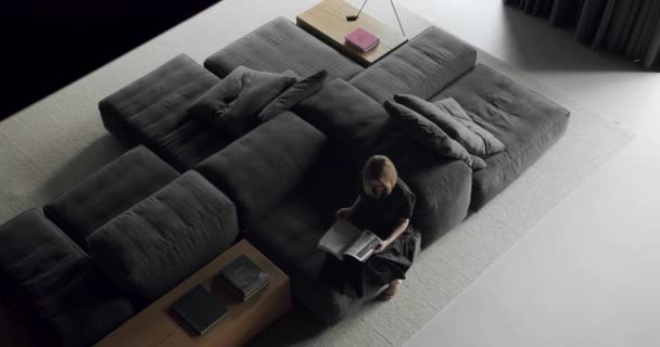 一个女人坐在沙发上看书 奢华的现代住宅与角落索法和书架 时尚的家具 简约家庭内部 舒适的现代家具设计 — 图库视频影像