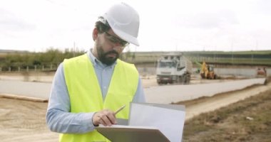 Male engineer in uniform and white helmet makes notes in notebook at work. Verification of works on the territory of the construction site. Industrial Building Construction Site. construction works .