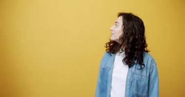 Happy young female with curly brown hair holding bank card and looking amazed with great credit provision showing thumb up on yellow background. Smiling woman promoting credit card. 