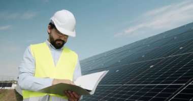 Male engineer inspecting solar panels. Positive adult man in uniform checking photovoltaic panels and making notes in journal during work on solar power station. checking the panels.