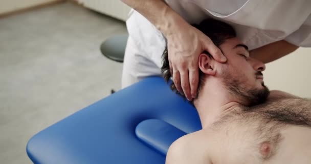 骨科诊所工作期间闭眼男性患者手持式作物疗法师旋转和伸长颈部的高角盘 — 图库视频影像