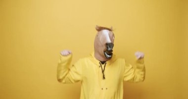 Excited man in horse mask jumping. Static shot of happy male in hoodie and horse mask raising clenched fists and jumping while celebrating success against yellow background.