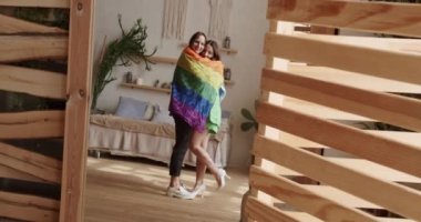 Lgbt women couple rest at home. Embrace and holding each other with pride rainbow flag. Romance and portrait of lesbian couple enjoying. LGBT rights, Lesbian family. Lifestyle and relationships.