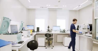Man working in clinic laboratory. Handheld shot of male medical specialist in uniform preparing samples and using analyzing machine during work in lab of modern hospital.
