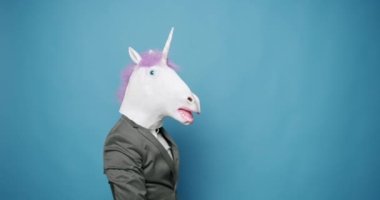 Fun and happiness concept. Funny Guy in Gray Suits Dance with Unicorn Mask, he is having fun on isolated Blue Background. Having Fun, Party Halloween. Slow Motion. April 1, Fools Day. Masquarade idea