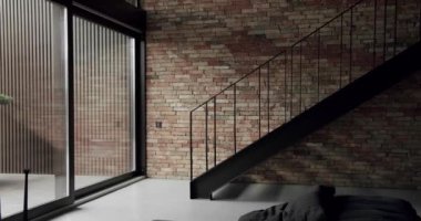 Siyah merdiveni ve geniş pencereleri olan modern bir dairede eski tuğla renkli bir duvar. Minimalist oturma odası ve tuğla duvar. Tuğla oda, iç yapı, merdivenli tuğla duvar arka planı..