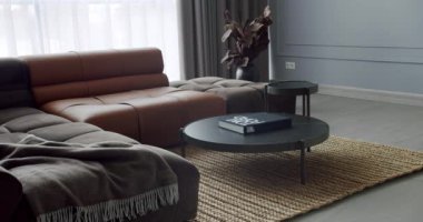 Gri ve kahverengi mobilyalı modern Minimalist oturma odası. Köşedeki kanepe ve yuvarlak masa. Moda mobilyalar. Minimalist İç İşleri. Konforlu Modern Mobilya Tasarımı