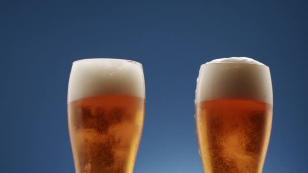 Two Glasses Full Frothy Beer Collide Middle Blue Background Foam — Stockvideo