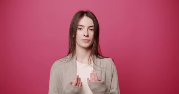 緊張した若い女性が説明する ピンクを背景にカメラに何かを説明しながら 黒髪のジェスチャーと話をスタイリッシュな服の中で不安若い女性 — ストック動画