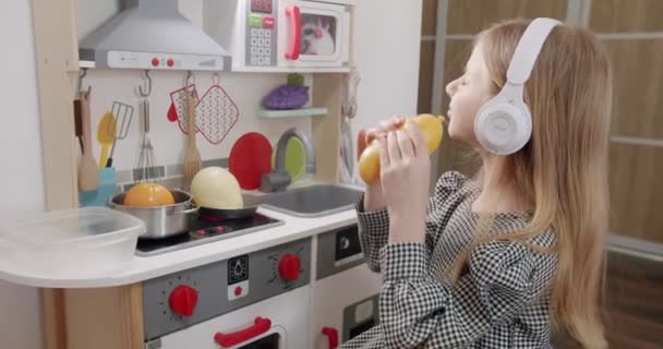 这个7岁的女孩正在儿童房里玩 她的耳机是白色的 听着音乐 积极玩现代玩具 听音乐 享受时间 — 图库视频影像