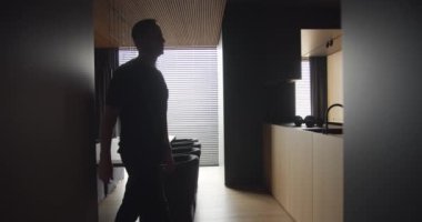 Silhouette A man in an apartment with an modern kitchen interior, The man walks through the kitchen. Modern Dining room with wood and minimalist design.