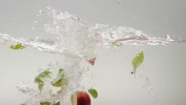 掉进干净的水里的苹果楔子 白色底色透明清澈水慢动作静态拍摄及落叶成熟红苹果片 — 图库视频影像