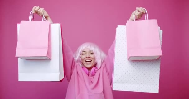 ピンク色のコンセプトでカラフルなバッグで買い物した後のハッピーガール 女性は割引と行われた購入を楽しんでいます ピンクの背景のスタジオのポートレートに隔離された成功した買い物の後 — ストック動画