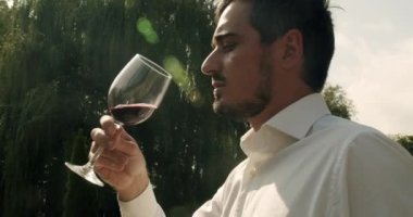 Positive sommelier mixing red wine in glass evaluating color at tasting. Man winemaker tasting wine. Concept of tasting and good life. Sommelier is shaking the glass of wine and tasting it.
