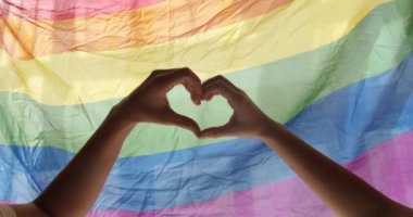 Gay and lesbian pride lgbt flag. Supporting hands make heart sign and wave in front of a rainbow flag flying. Love sign. Celebration Event Symbol Of LGBT. Love Equal. LGBT rights. human relationships.