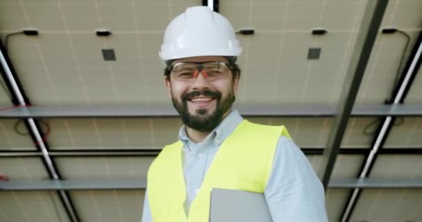 ポジティブな技術者は 太陽電池パネルの分野を通して太陽電池ファームの後ろにカメラと笑顔を見て 太陽電池は将来の重要な再生可能エネルギーになります — ストック動画
