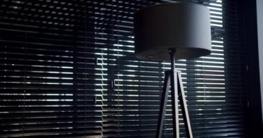 Modern black lamp inside. Black minimalist circular floor lamp next to a window with modern black blinds. Minimalist Interior with lighting equipment. Contemporary modern lamp. Luxury Chandelier.