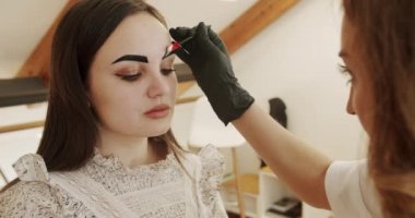 Eyebrow tinting procedure with henna in a beauty salon. Cosmetology procedure. A beautician does henna eyebrow tinting for the young woman, cosmetological procedures and beautycare.