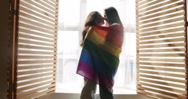 Çifti kucaklayın, gülümseyin ve bayrak sallayın. Sevgiler ve öpücükler, LGBT hakları, lezbiyen ailesi. Sevgi ve desteği paylaşan iki kadın el ele tutuşuyor. Yaşam tarzı ve ilişkiler.